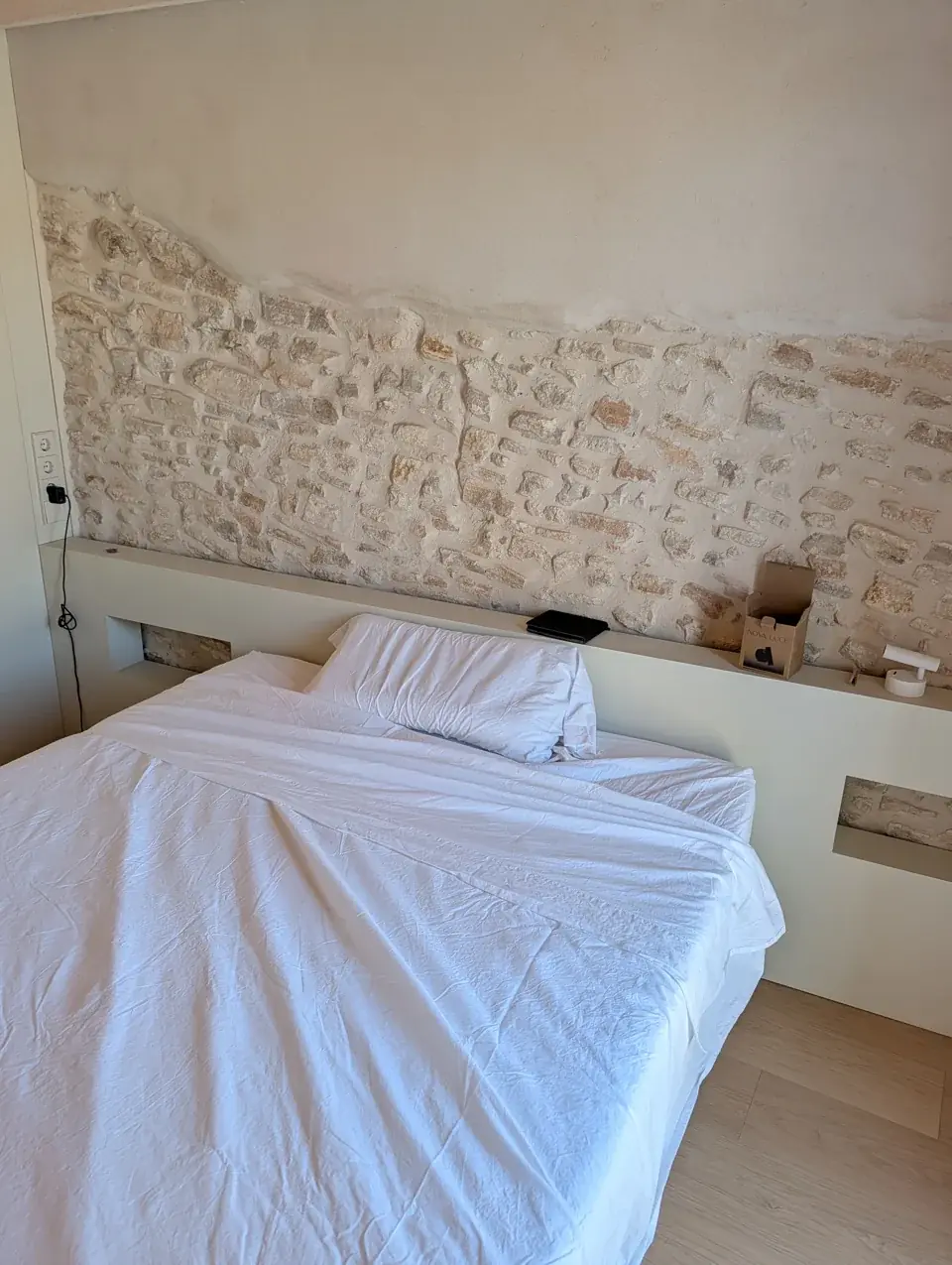 Cama junto a un muro de piedra bajo un techo de madera