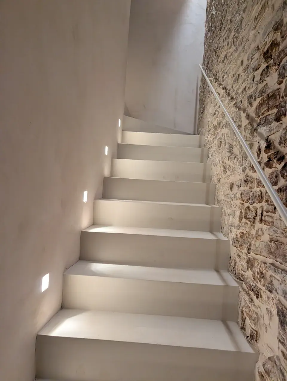 Escalera clara iluminada junto a un muro de piedra