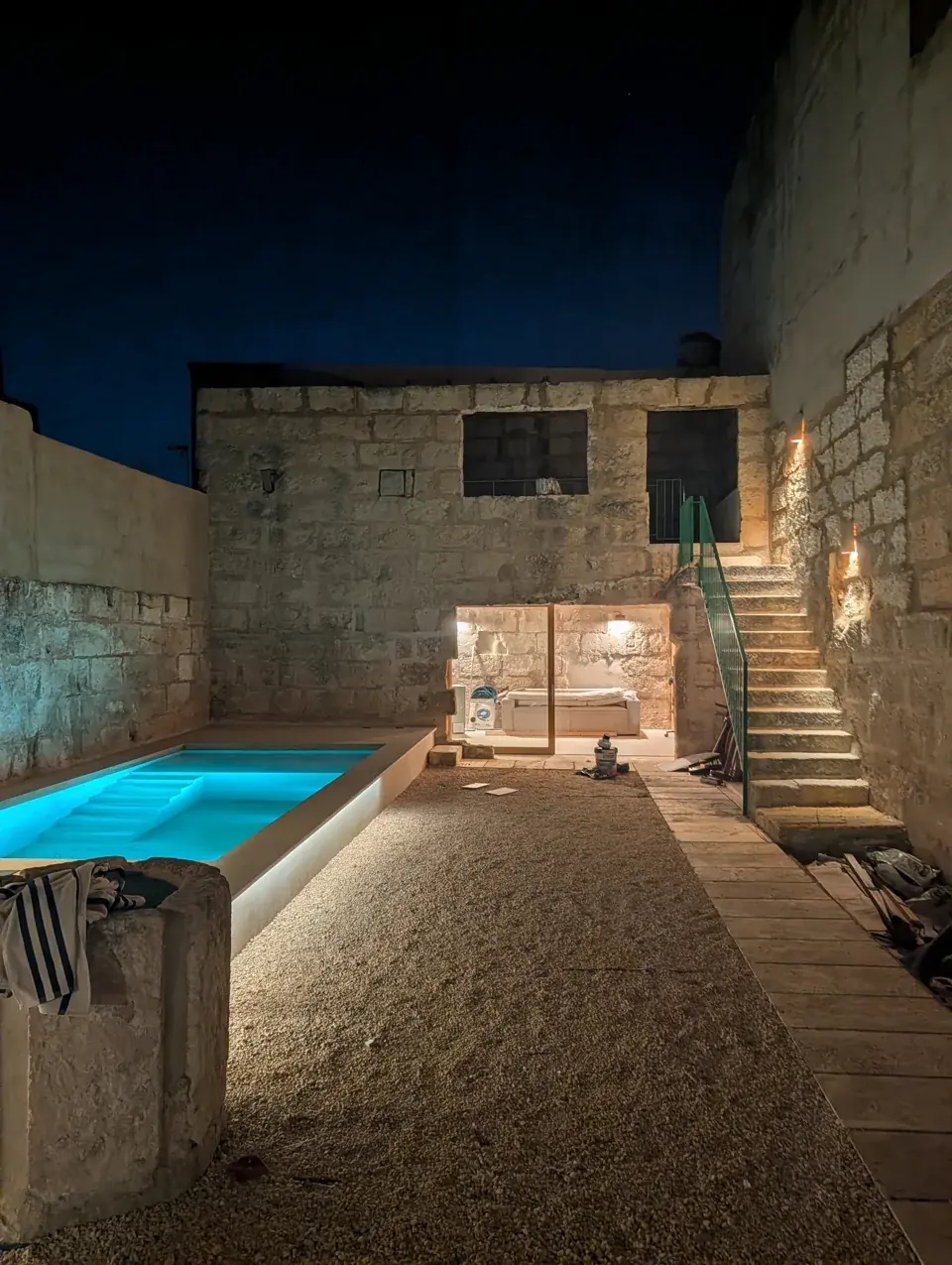 Patio con la piscina iluminada entre muros de piedra, de noche