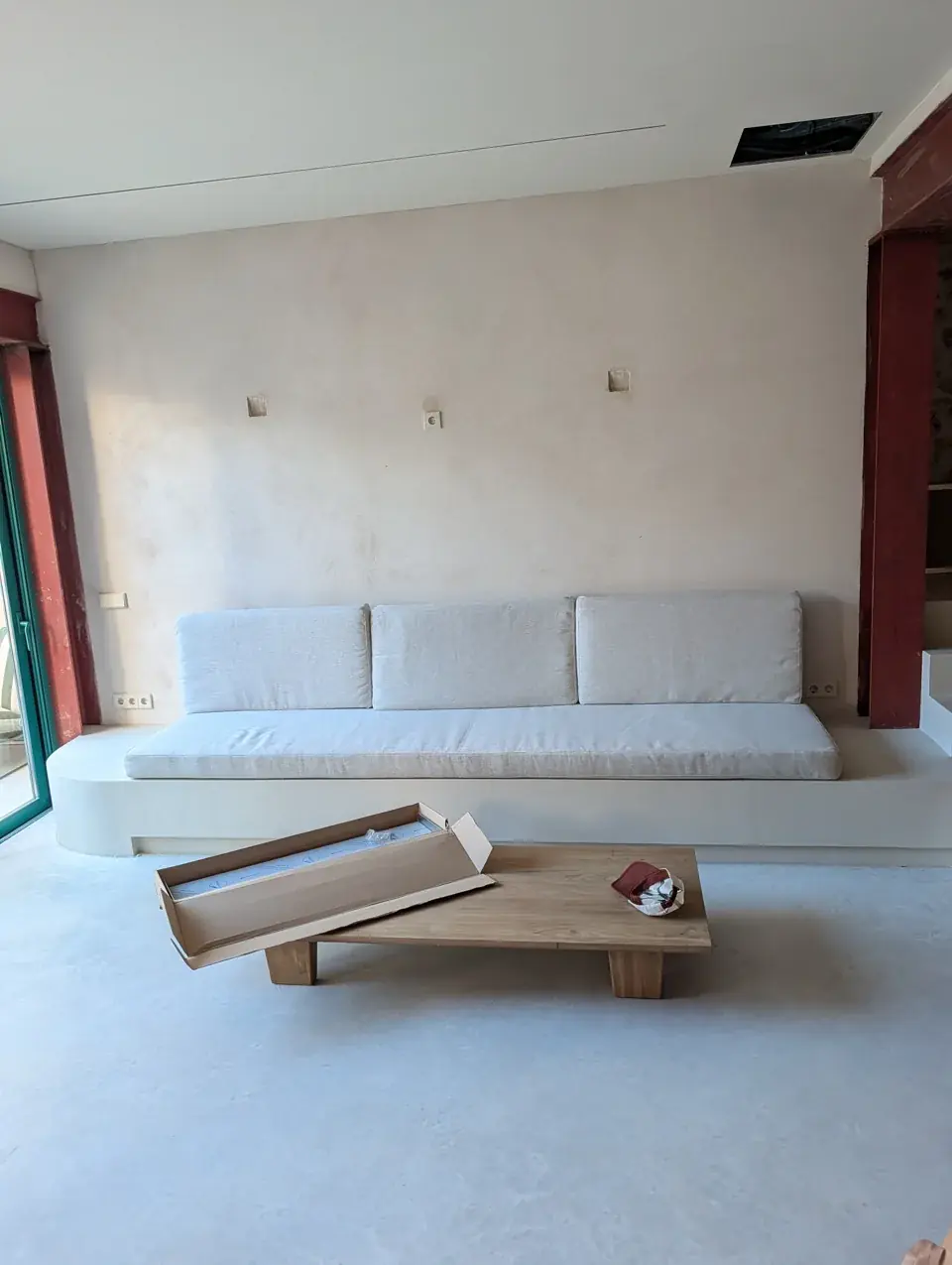 Salón con banco de obra, mesa baja de madera y cristalera al patio